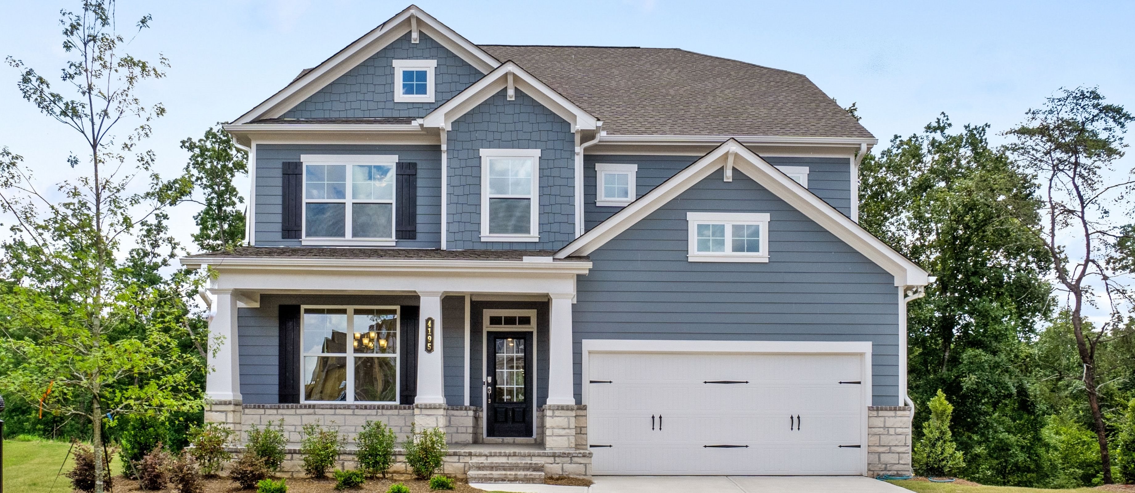 A single-family, 2-story home with muted blue exterior with light grey stone accents. The home is surrounded by lush greenery.