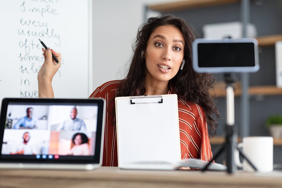 A woman teachers in front of a white board while being recorded by a tablet