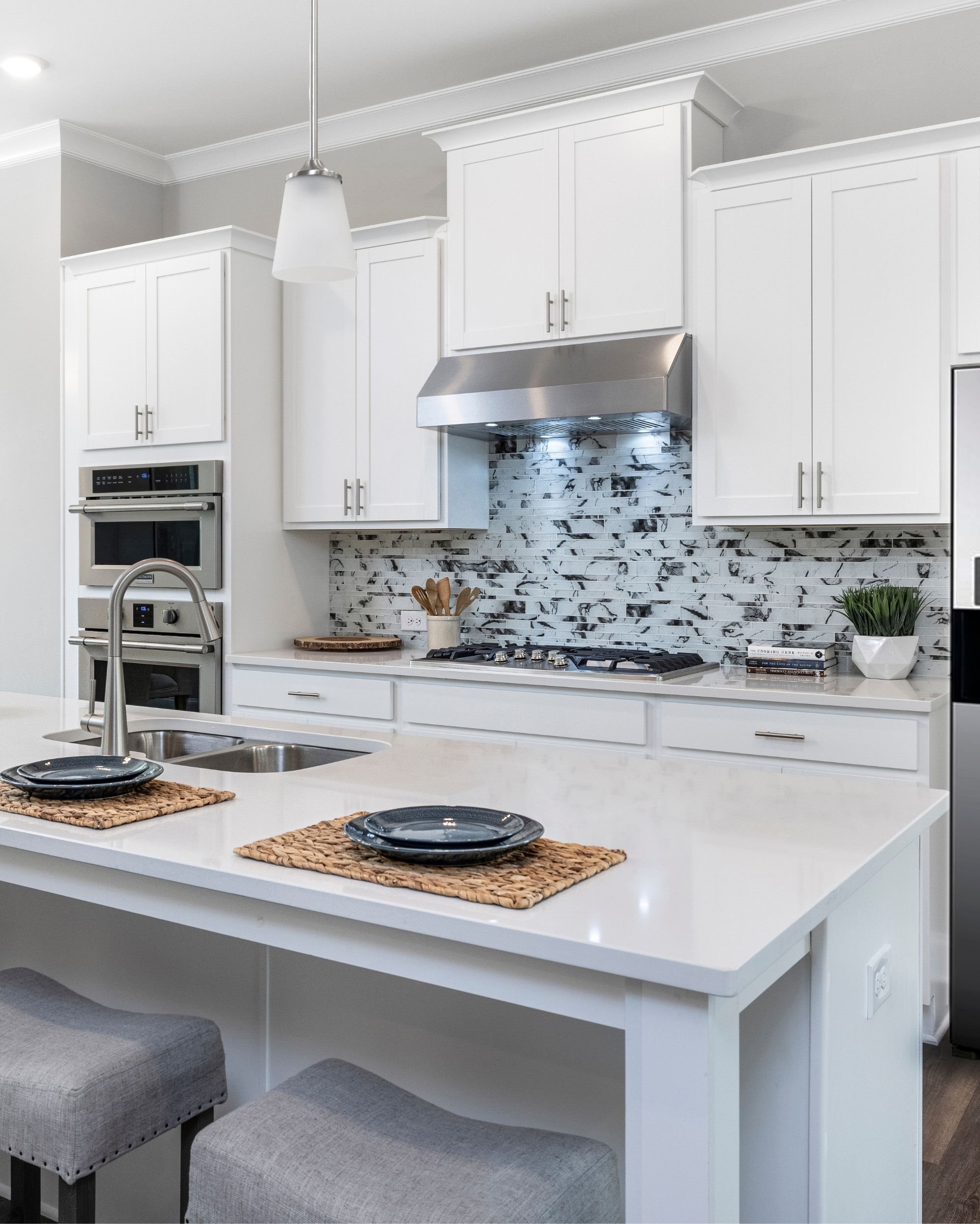 White kitchen with double ovens and a gas stove with hood. A generous center island is set up with placemats and plates, perfect for a family breakfast before running out the door. 